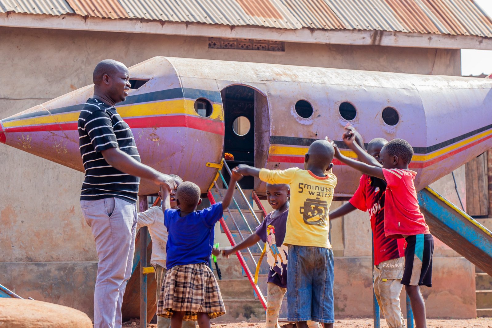 A Streams of Joy Services worker and a group of children holding hands in a circle beside a painted aeroplane play structure