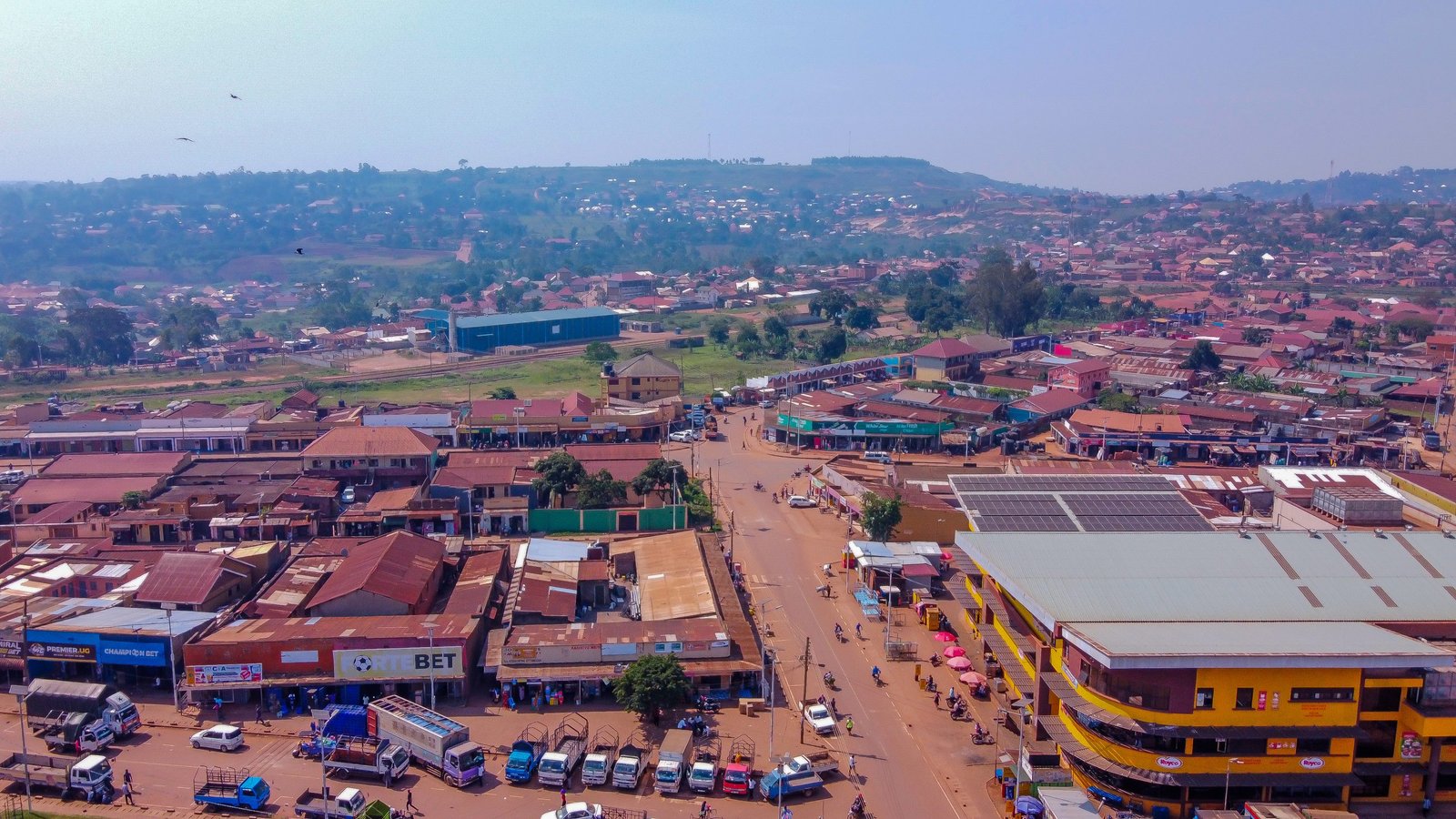 An aerial view over the trading centre and rooftops of a Ugandan town, with hills on the horizon