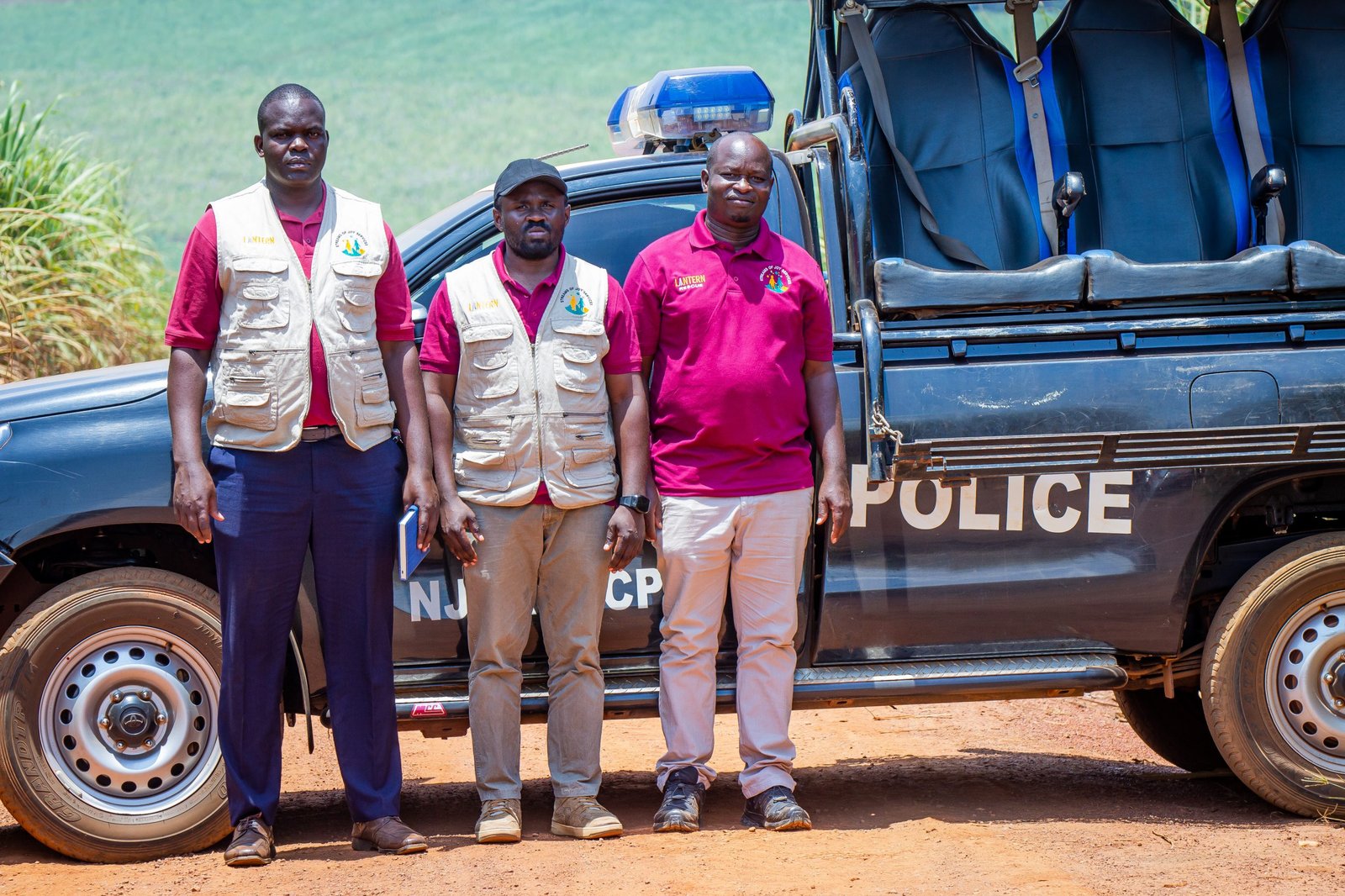 Three Streams of Joy Services officers in branded vests standing beside a Uganda Police pickup on a field track